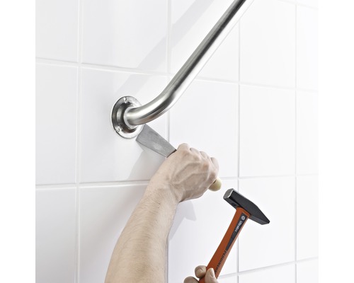 En person tar bort ett stödhandtag från väggen med hammare och mejsel.