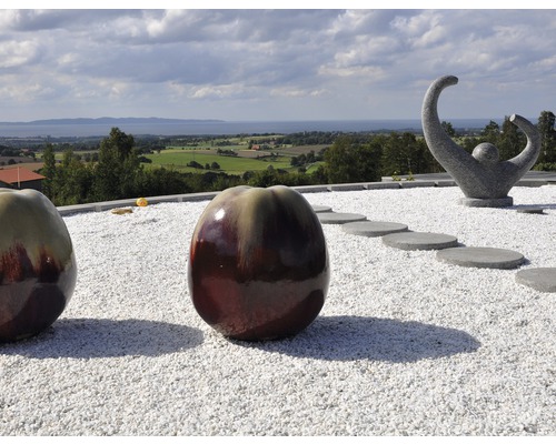 Trädgårdsscen med dekorativa keramikfrukter, stenskulptur och grusyta