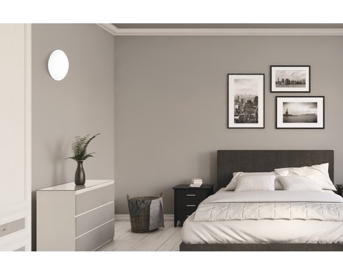 Sovrum med säng, byrå, sängbord, vägglampa och tavlor