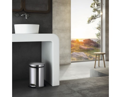 Modernt badrum med tvättställ, vitt tvättställsskåp och en rund metallisk pedalhink