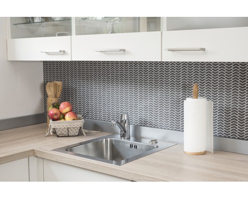 Diskho i rostfritt stål med blandare och köksredskap på en ljus bänkskiva framför en mörk mönstrad bakgrund