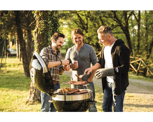 Tre män grillar korv och kött på en klotgrill utomhus.