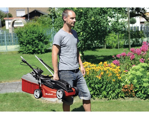 En man bär en Einhell gräsklippare genom en trädgård.