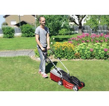 Man klipper gräsmattan med en röd Einhell gräsklippare i trädgården.