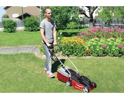 Man klipper gräsmattan med en röd Einhell gräsklippare i trädgården.