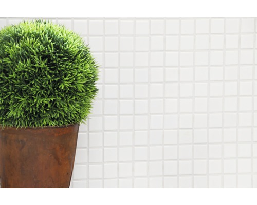 Dekorativ konstväxt i kruka framför en vit mosaikbakgrund