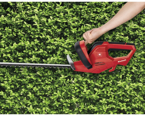 Enhandsmanövrering av en röd Einhell häcksax framför en grön häck.