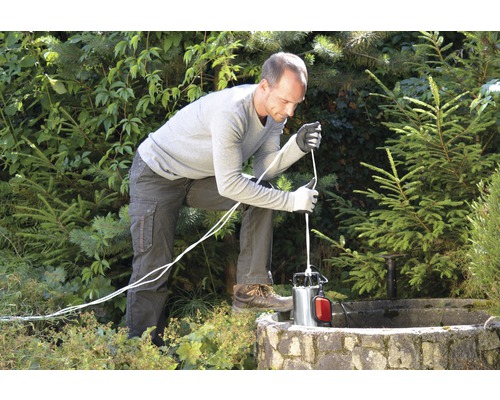 En man sänker ner en djupbrunnspump i en brunn