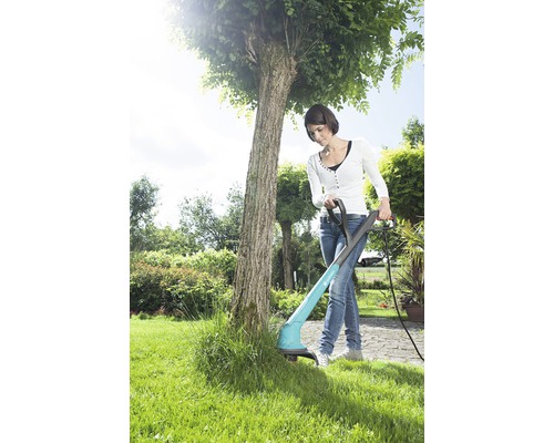 Kvinna använder en grästrimmer i trädgården för att klippa gräs.