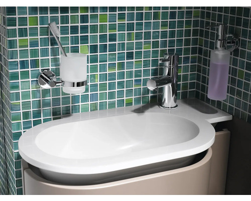 Tvättställ i badrum med armatur, tvålpump och tandborstmugg framför kakelvägg