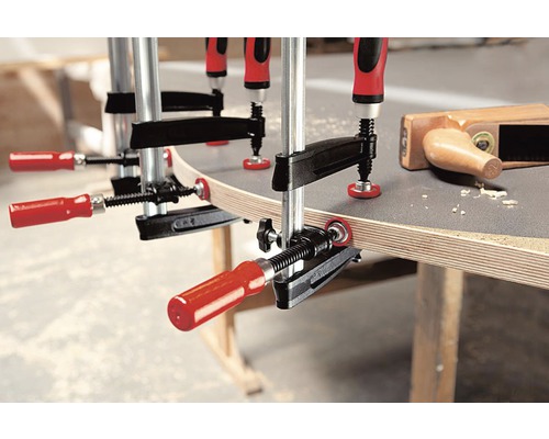 Flera skruvtvingar fixerar ett arbetsstycke på en arbetsbänk.