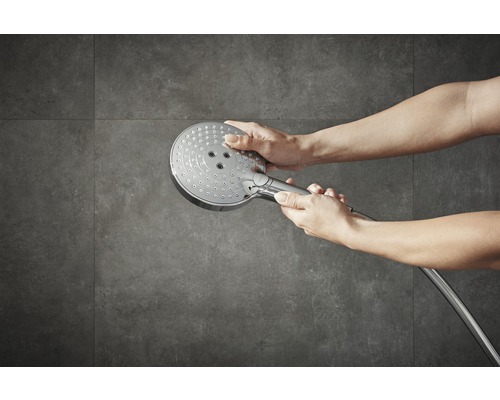 Person håller ett duschhuvud framför en grå vägg