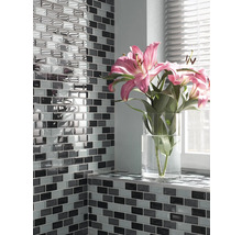 Vägg med rektangulära mosaikplattor och blommor i en vas på fönsterbrädan