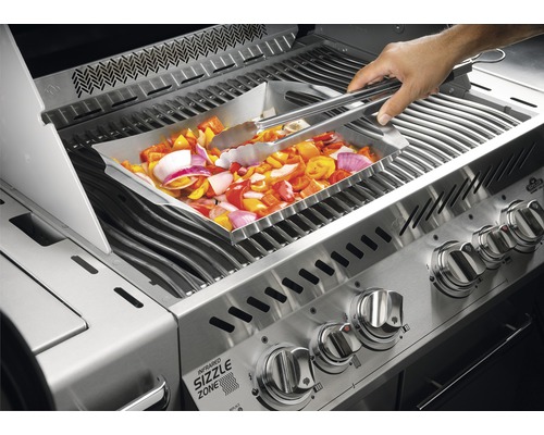 Grönsaker vänds med tång i ett grilltråg på en gasolgrill.