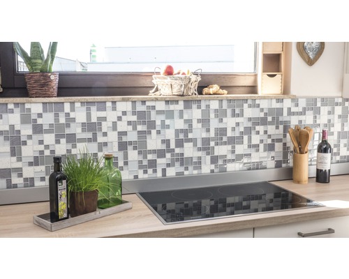 Köksscen med mosaikplattor på väggen och kokplatta på bänkskivan.