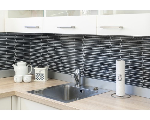 Köksscen med diskho, kran, bänkskiva, porslin och köksredskap mot en svart mosaikvägg