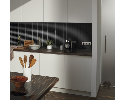 Köksvy med bänkskiva, köksredskap och elektriska apparater framför en mosaikplattvägg