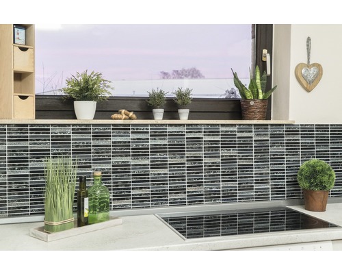 Köksscen med mosaikplattor på väggen, växter och köksredskap på arbetsbänken.