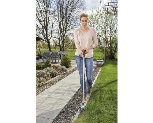 Kvinna använder en gräskantsskärare i trädgården för att klippa gräskanterna.