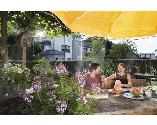 Ett par sitter vid ett träbord i trädgården under ett parasoll och äter vattenmelon.