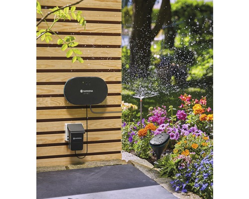 Scen med Gardena bevattningssystem med bevattningsdator, sensor och sprinkler i en trädgård med en blomsterrabatt