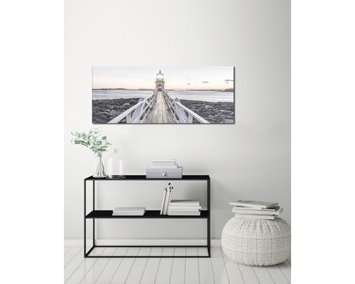 Dekorativ väggbild med en fyr vid havet ovanför en svart konsol