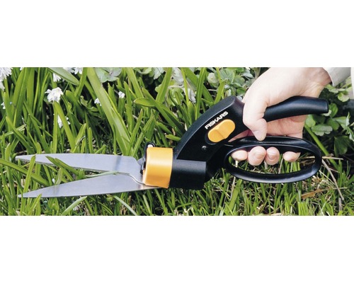 En person klipper gräs med en grässax från Fiskars.