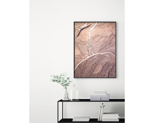 Inramad väggkonst med flygfoto över väg i ökenlandskap ovanför en hylla