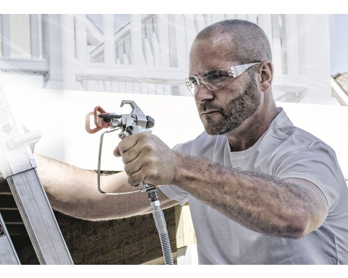 En man använder en färgspruta för målningsarbeten utomhus.