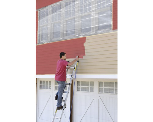 Man målar husfasaden med färgspruta från en stege. Fönstren är täckta med plast.