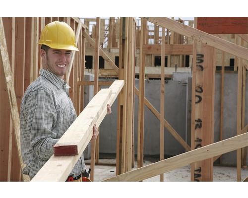 En byggnadsarbetare med skyddshjälm håller träribbor på en byggarbetsplats.