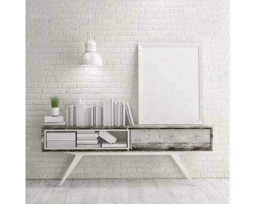 Dekorativ interiör med konsolbord, böcker, krukväxt, lampa och bildram framför en tegelvägg