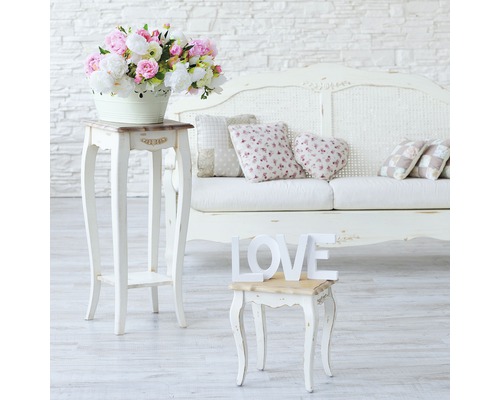 Dekorativ interiör med blomsterarrangemang, sidobord, kuddar och soffa.