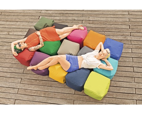 Två kvinnor kopplar av på en hög med fyrkantiga kuddar utomhus.