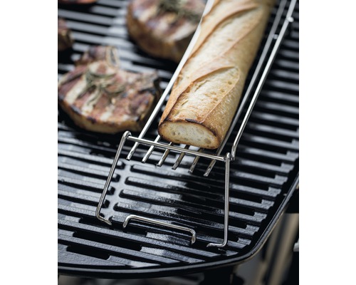 Baguette i en grillbrödshållare i rostfritt stål på en grill med grillad mat