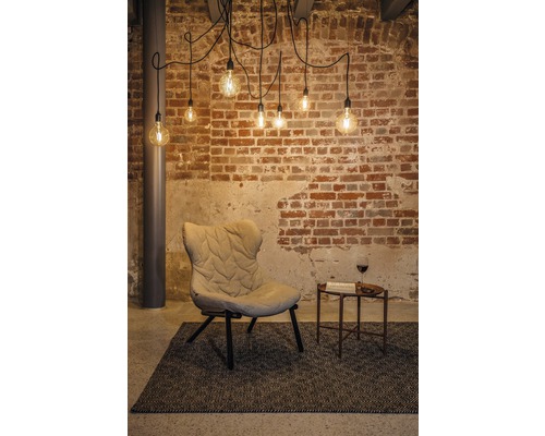 Inredningsidé med fåtölj, sidobord, matta och pendellampa framför en tegelvägg