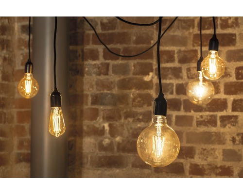 Flera glödlampor med glödtrådar hänger framför en tegelvägg.