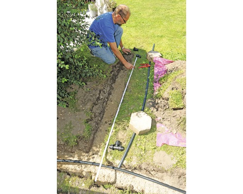 Man mäter bevattningssystem i trädgården med en tumstock.