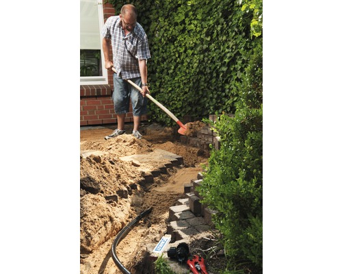 Man arbetar med en spade i trädgården på en mur av gatstenar