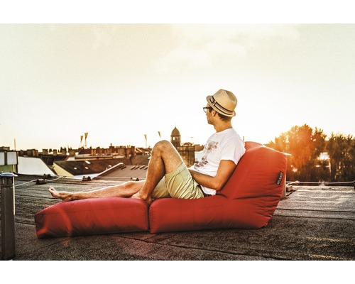 Man med hatt kopplar av på en röd sittsäck med fotstöd på ett tak