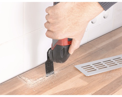 En person använder ett multifunktionsverktyg för att skära en träpanel nära en vägg