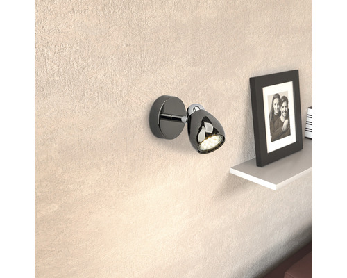 Svart vägglampa med LED-ljus och justerbart huvud bredvid en hylla