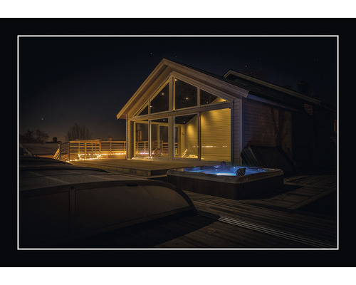 Utomhusvy av ett hus med bubbelpool och träterrass på natten