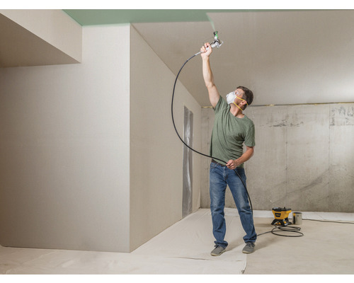 Man målar taket med färgspruta i ett rum.