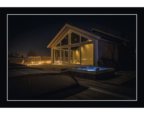 Utomhusbadtunna bredvid ett hus med stora fönster på en träterrass på natten