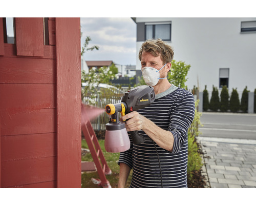 Man målar trä med färgspraysystem och andningsskydd