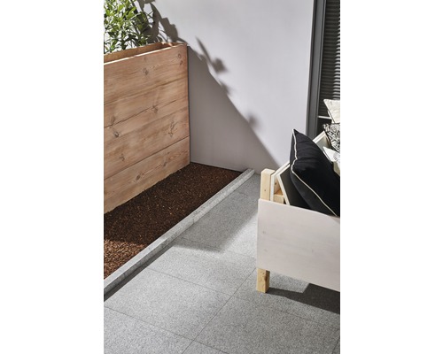 Miljö med träplanteringslåda, sittplats och gråa terrassplattor.