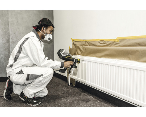 En person lackerar ett element med en färgspruta, täckt med maskeringstejp och papper.