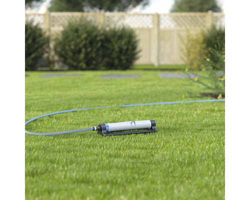 Trädgårdssprinkler med slang på gräsmatta