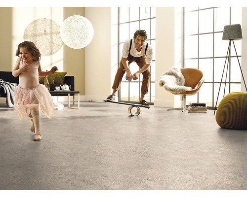 Ljust vardagsrum med golvbeläggning, där en man står på en balansbräda och ett barn springer runt